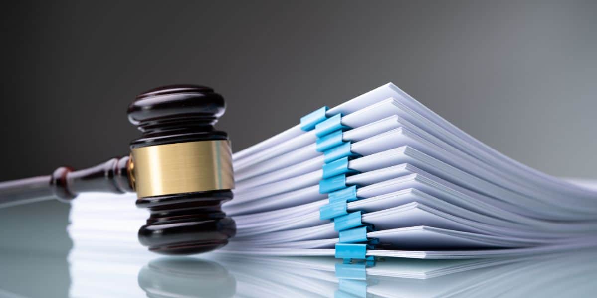 Judge's gavel next to a large stack of documents with blue clips