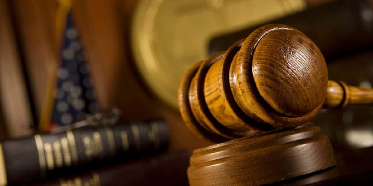 Close-up of a judge's gavel on a wooden stand with a blurred background of legal books and the American flag.