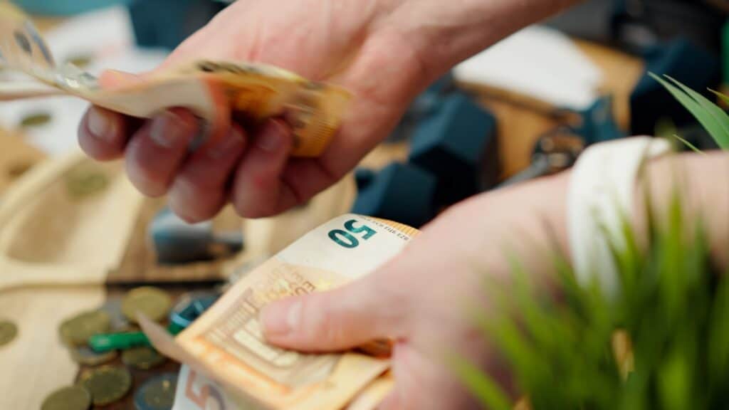 Real estate professional sits at a modern desk, thoughtfully looking at a calculator next to a small amount of cash, repre...
