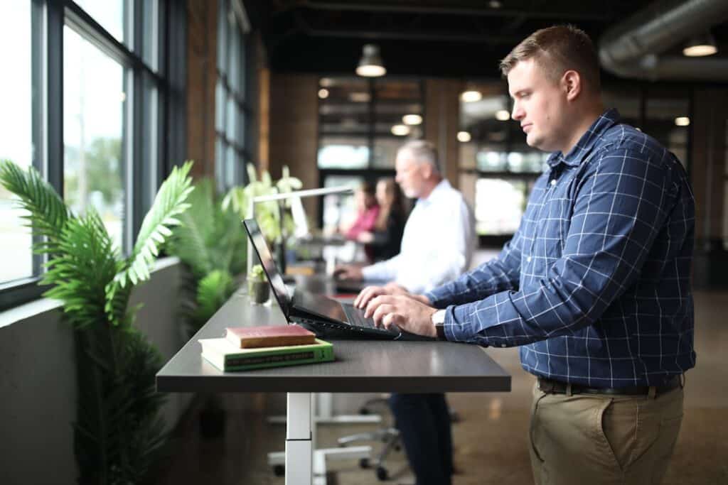 Confident real estate franchise owner stands in a bright, modern office, looking thoughtfully out a large window at the ci...
