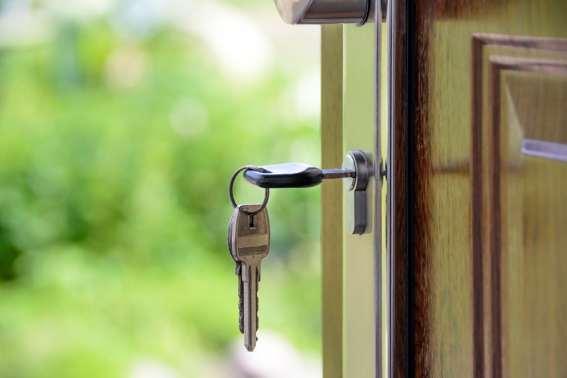A single, professional real estate agent stands confidently in front of a modern house, holding a set of keys, representing financial independence and success.