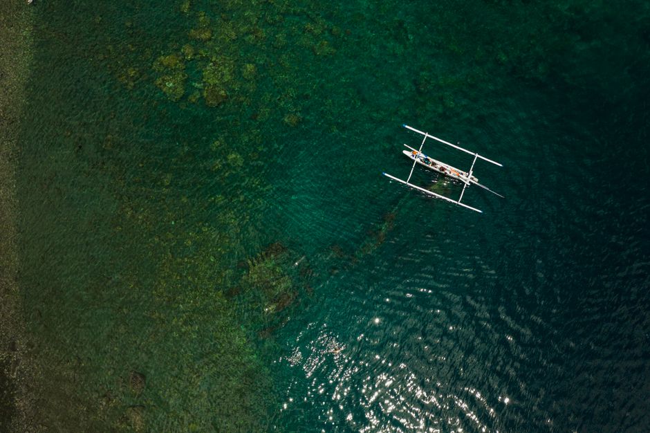 Aerial drone shot of a single boat sailing on a vast, calm, deep blue ocean, representing a clear and uncontested market s...