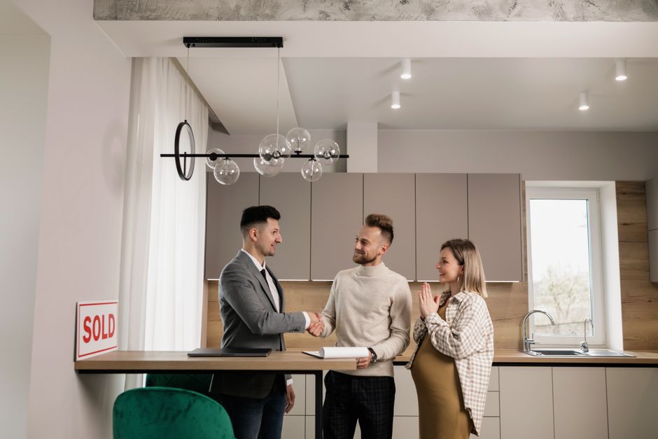 A confident, modern real estate broker shakes hands with a happy client in a bright, beautiful home, representing a successful partnership without commission friction.