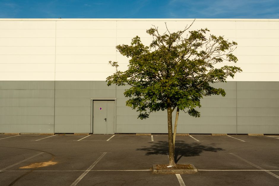 Eye-level shot of a large, abandoned big-box store with a crumbling facade and an empty parking lot, symbolizing an obsole...