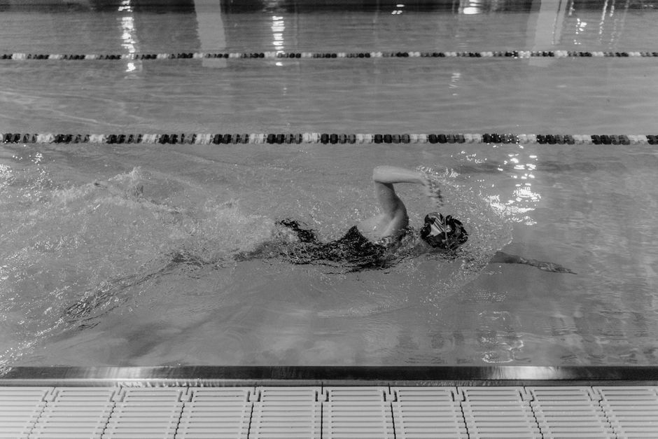 A single person swimming in their own lane in a large, empty, modern swimming pool, symbolizing freedom from competition and a clear path forward.