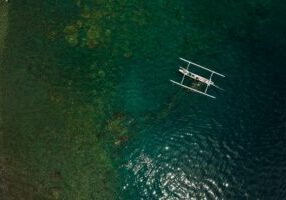 Aerial drone shot of a single boat sailing on a vast, calm, deep blue ocean, representing a clear and uncontested market s...