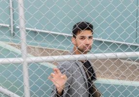Well-dressed real estate agent decisively opens a large, modern gate, symbolizing smashing barriers to brokerage ownership.